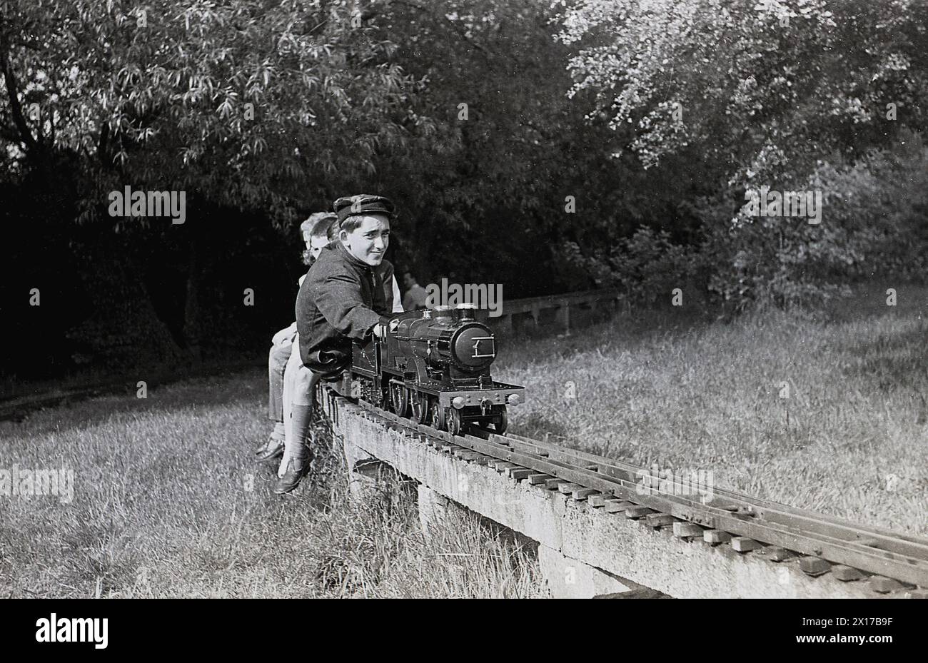 Anni '1970, storico, estivo e all'aperto in un campo, su un binario ferroviario sopraelevato, un macchinista che offre ai bambini un giro su una ferrovia a vapore in miniatura, Inghilterra, Regno Unito. Foto Stock