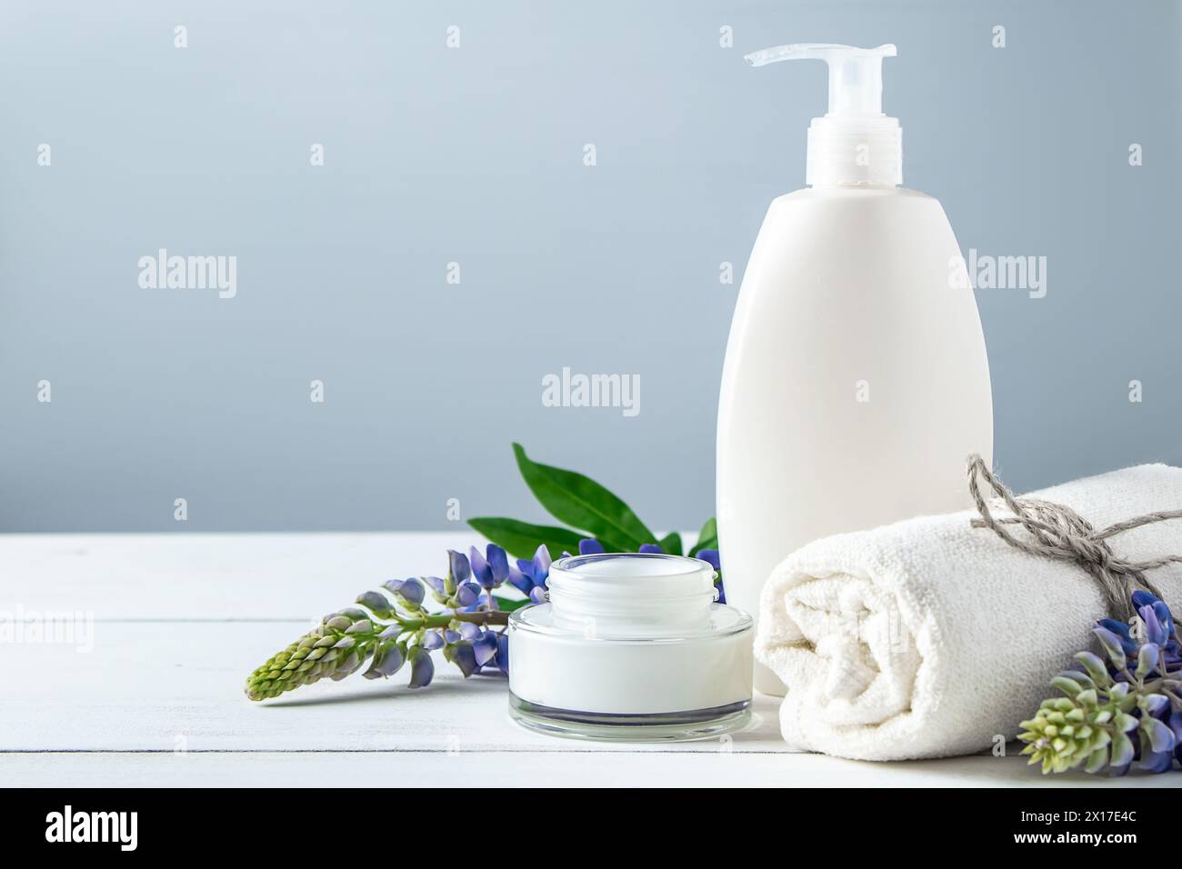 Bottiglia cosmetica con lozione e fiori lupino su sfondo grigio. Cosmetici naturali per la cura del corpo e del viso. Concetto di prodotti biologici spa, relaxati Foto Stock