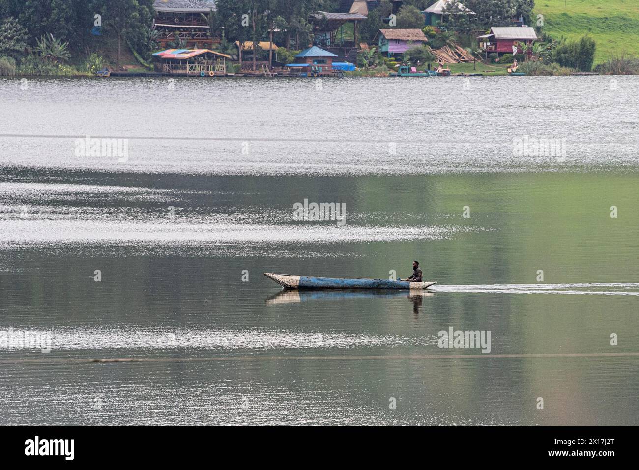 Catturata in serena solitudine, una canoa blu intemprata naviga con grazia nelle tranquille acque del lago Bunyonyi, incorniciata dalla pittoresca bellezza di Uga Foto Stock