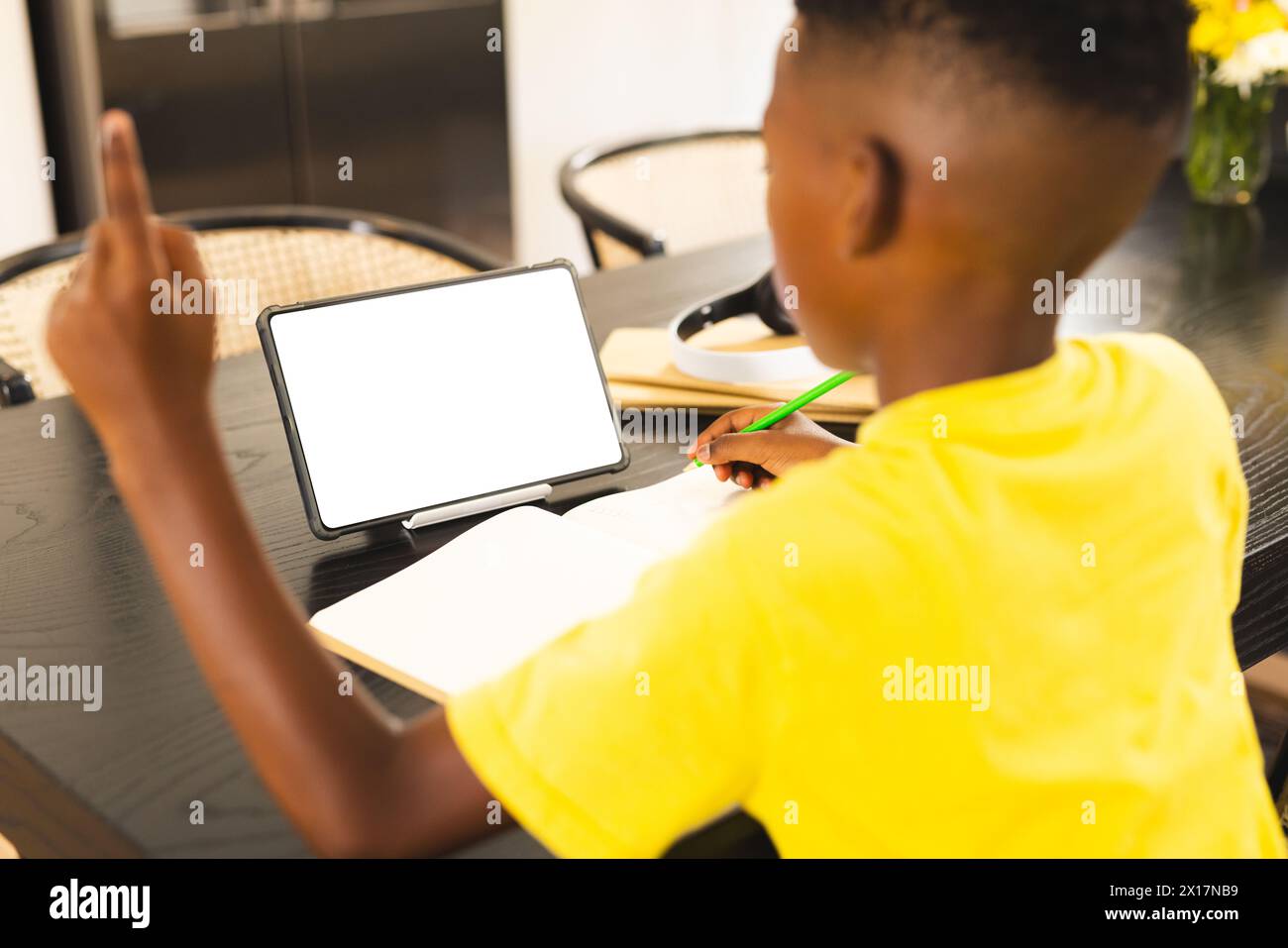 Ragazzo afroamericano che si concentra sulla scrittura a casa con spazio per le copie, tablet con schermo vuoto nelle vicinanze. Ha i capelli neri corti, indossa una camicia gialla, unale Foto Stock