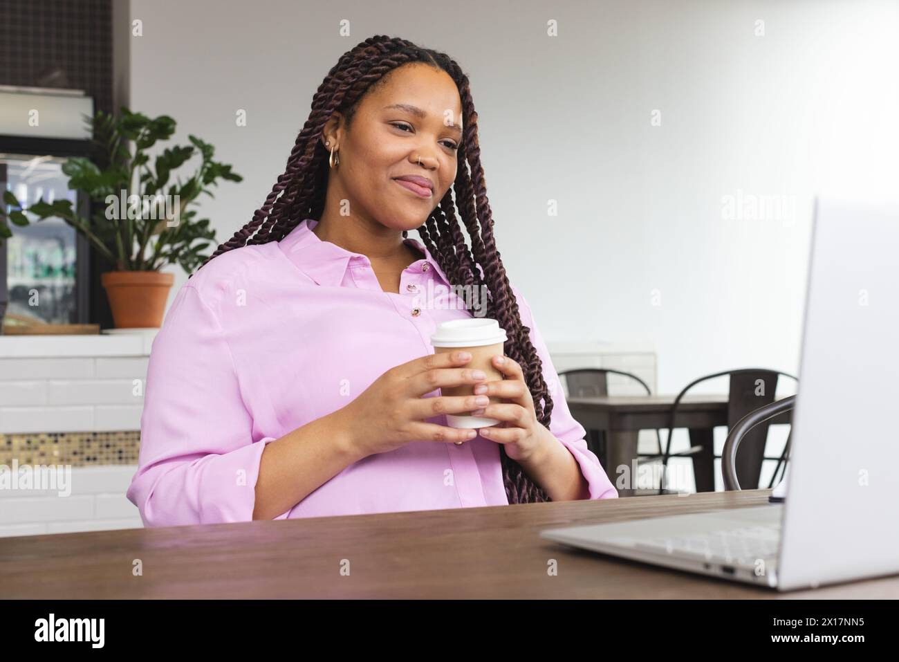 Donna birazziale che tiene il caffè, guarda un notebook Foto Stock