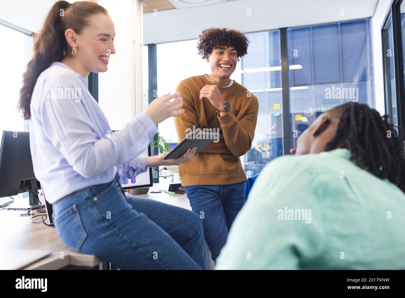 Team eterogenei che discutono su un tablet in un moderno ufficio aziendale, un uomo afroamericano che ascolta. Donna caucasica che tiene la tavoletta, uomo birazziale explaini Foto Stock