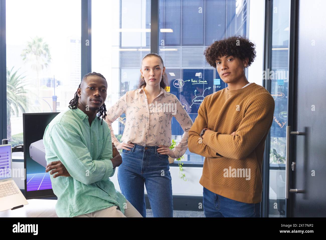 Team diversificato in ufficio, che guarda la fotocamera. Uomo afro-americano che indossa una camicia verde, donna caucasica con camicetta a motivi geometrici, uomo birazziale in una Foto Stock