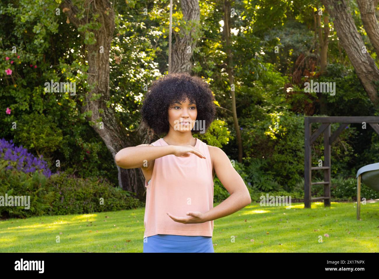 Giovane donna birazziale con capelli neri ricci che pratica yoga in giardino a casa Foto Stock