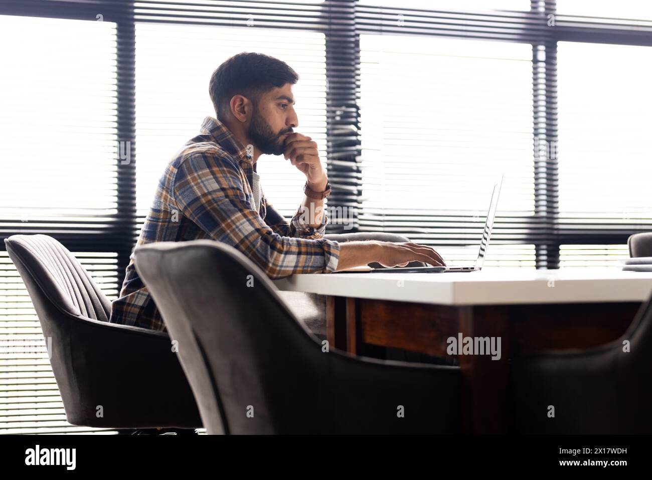 Giovane professionista asiatico seduto alla scrivania, guardando un notebook in un moderno ufficio aziendale Foto Stock