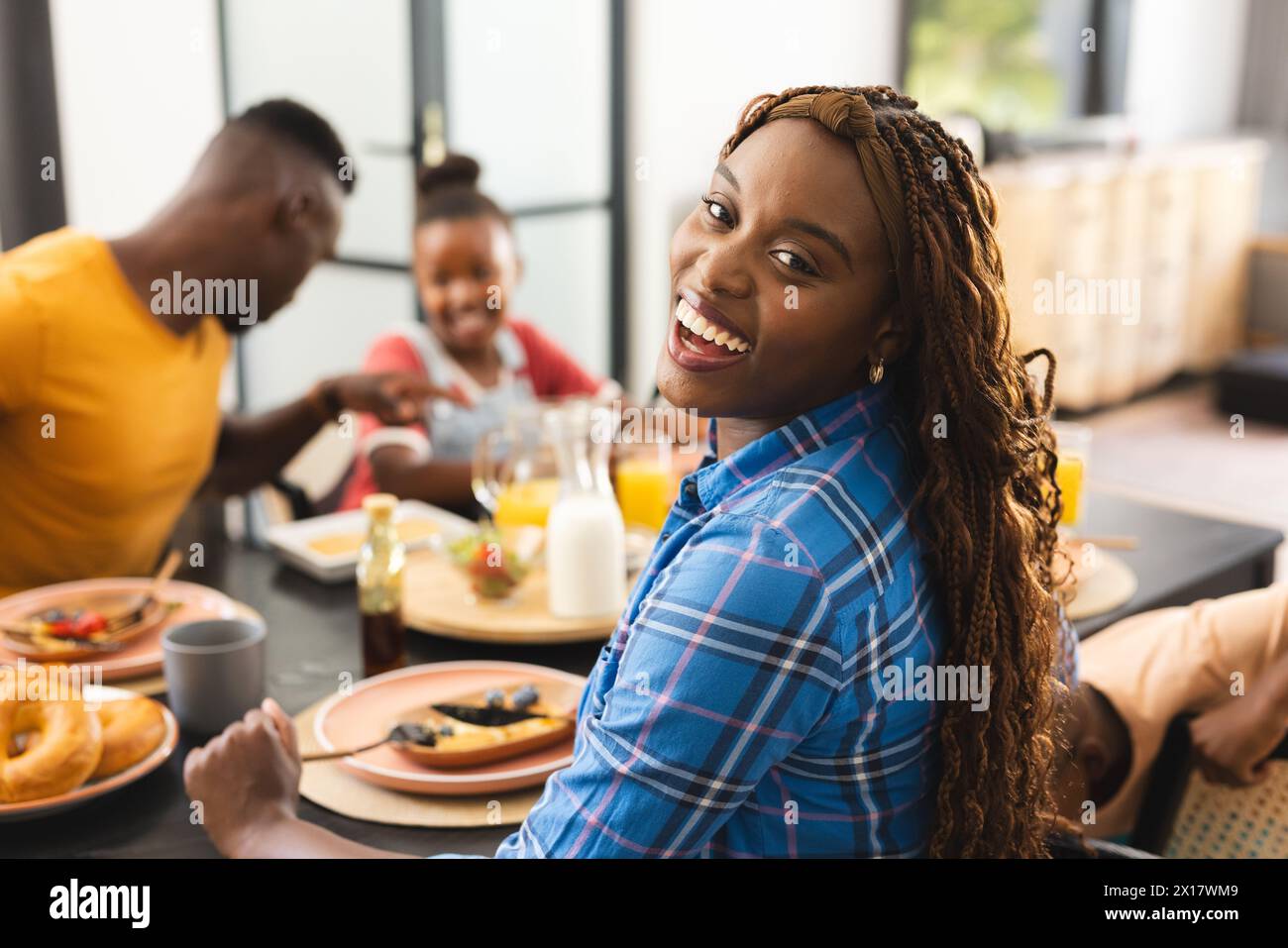 La famiglia afroamericana si gode la colazione a casa, la giovane donna sorride alla macchina fotografica Foto Stock
