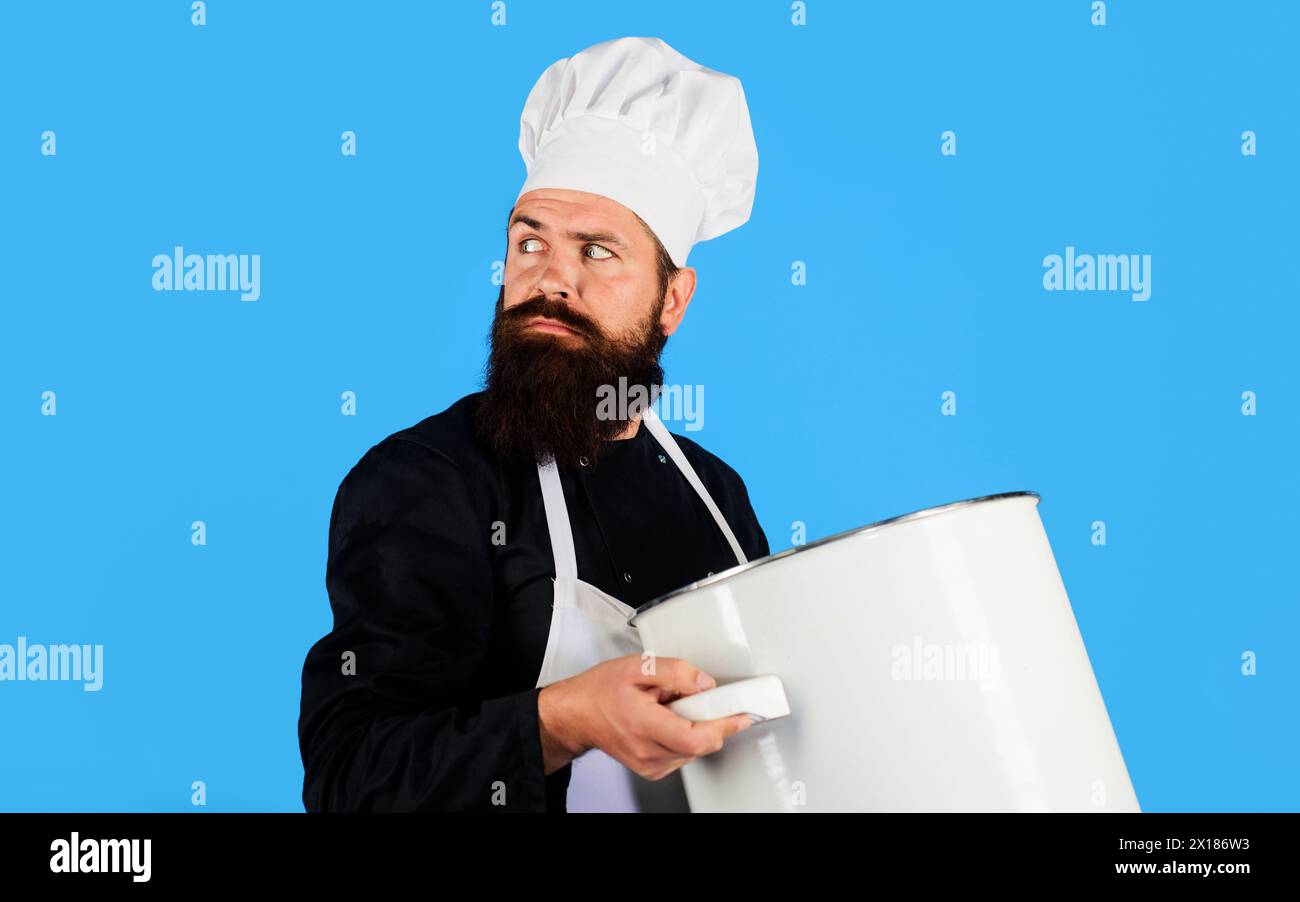 Cucina e cucina. Uomo barbuto serio con cappello da chef e uniforme con casseruola o casseruola. Pentole, stoviglie, utensili da cucina e utensili da cucina Foto Stock