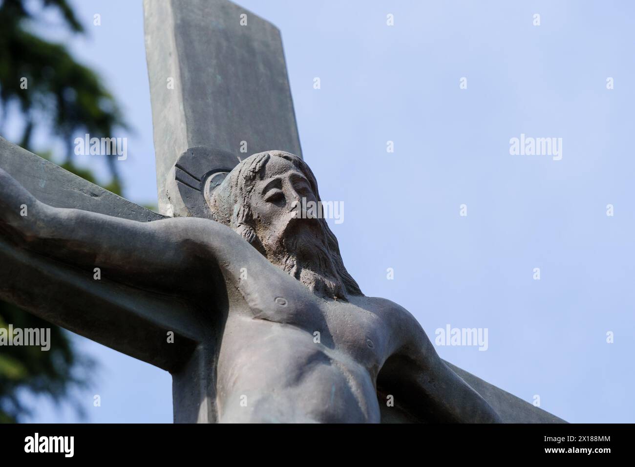 Scultura di Gesù Cristo crocifisso ambientata su uno sfondo blu del cielo con spazio copiato, foto ravvicinata. Foto Stock