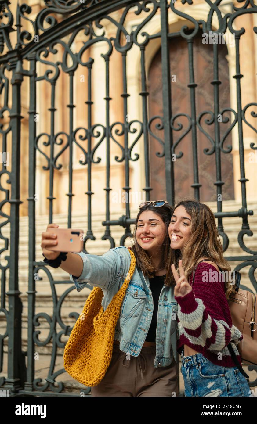 Due ragazze turistiche caucasiche sorridono e si fanno un selfie di fronte alla cattedrale di Malaga. Foto Stock