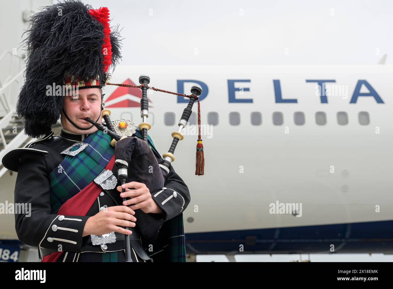Un piper in abito delle Highlands suona le cornamuse accanto a un jet della Delta Air Lines all’aeroporto di Edimburgo per celebrare il lancio del servizio estivo giornaliero tra Edimburgo e Atlanta, Scozia, Regno Unito Foto Stock