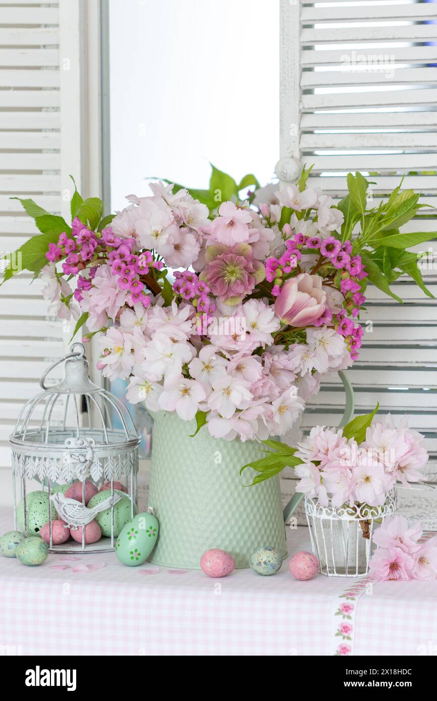 Accordo pasquale con un bouquet di ciliegie giapponesi in fiore, rose di quaresima, tulipani e bergenia e uova di pasqua Foto Stock