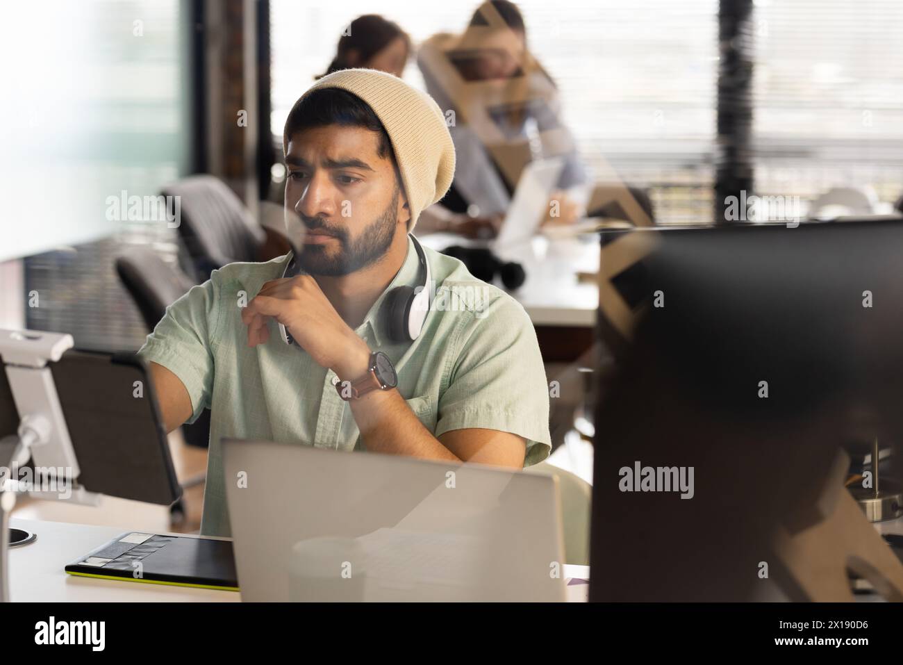 Uomo asiatico giovane professionista che guarda lo schermo di un tablet, nel profondo del pensiero, in un moderno ufficio aziendale Foto Stock