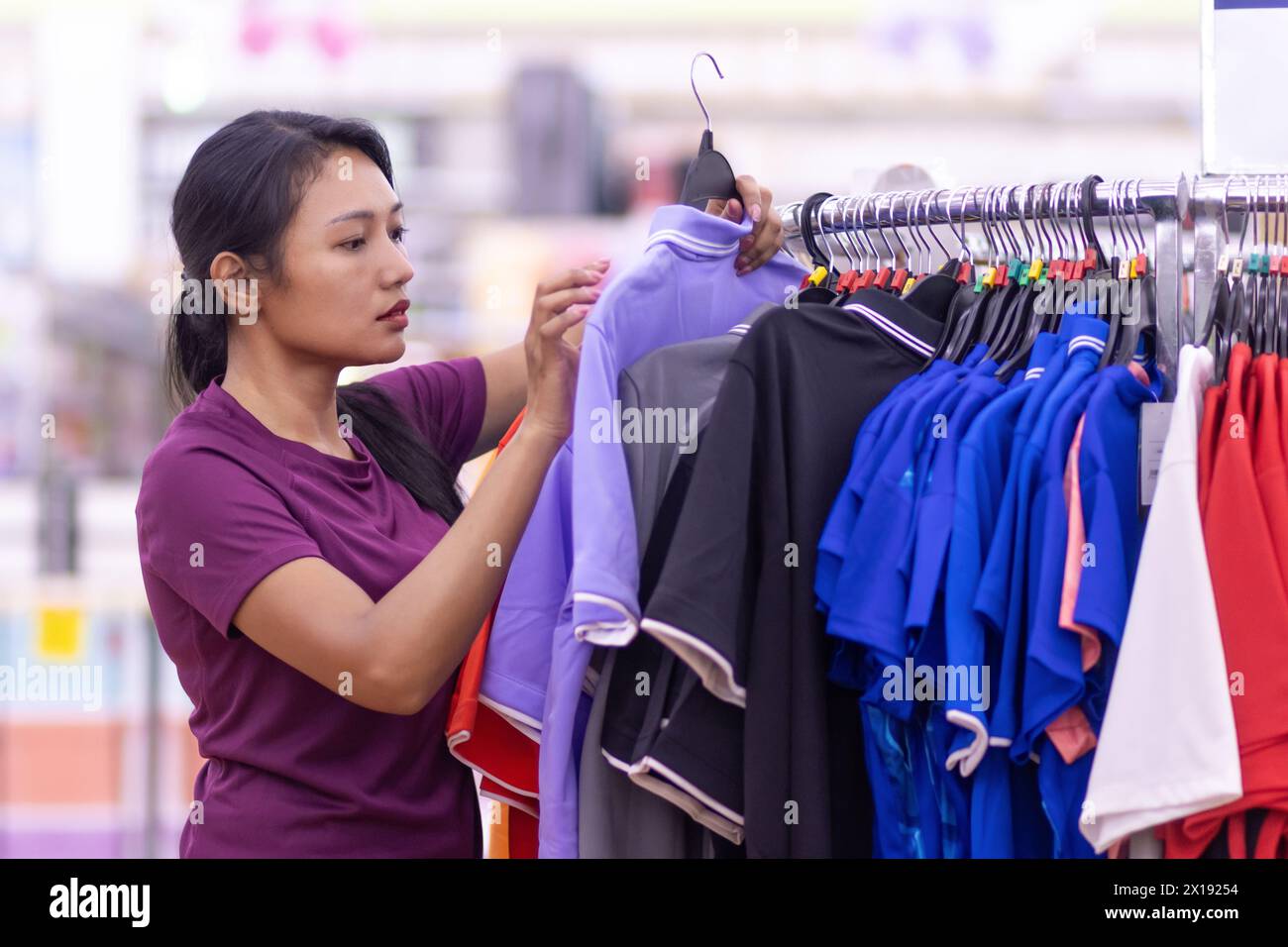 Una giovane donna sceglie una t-shirt in un negozio Foto Stock