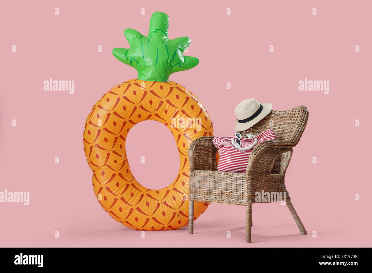 Anello gonfiabile a forma di ananas e poltrona in paglia con borsa e cappello su sfondo rosa Foto Stock