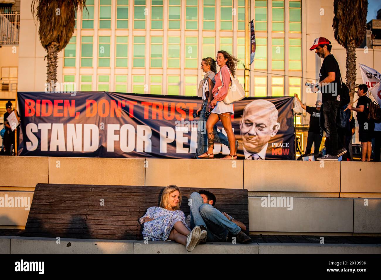 Tel Aviv, Israele. 15 aprile 2024. Una coppia israeliana si siede sotto uno striscione che chiede al presidente degli Stati Uniti Joe Biden di impedire al primo ministro israeliano Benjamin Netanyahu di attaccare l'Iran durante una manifestazione. Israele ha promesso di "determinare un prezzo” dall'Iran dopo un attacco senza precedenti su larga scala con drone e missili nel fine settimana che ha intensificato le tensioni regionali innescate dalla guerra a Gaza. (Foto di Eyal Warshavsky/ SOPA Images/Sipa USA) credito: SIPA USA/Alamy Live News Foto Stock