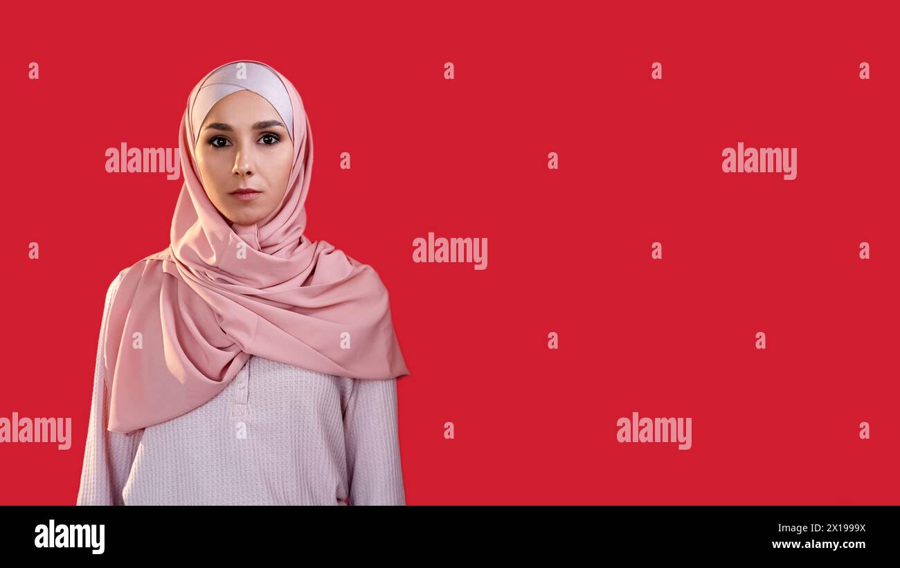 Faccia spaventata. Paura dell'ansia. Shock di panico. Ritratto di una donna spaventata e sopraffatta in hijab isolata su uno sfondo rosso vuoto. Foto Stock