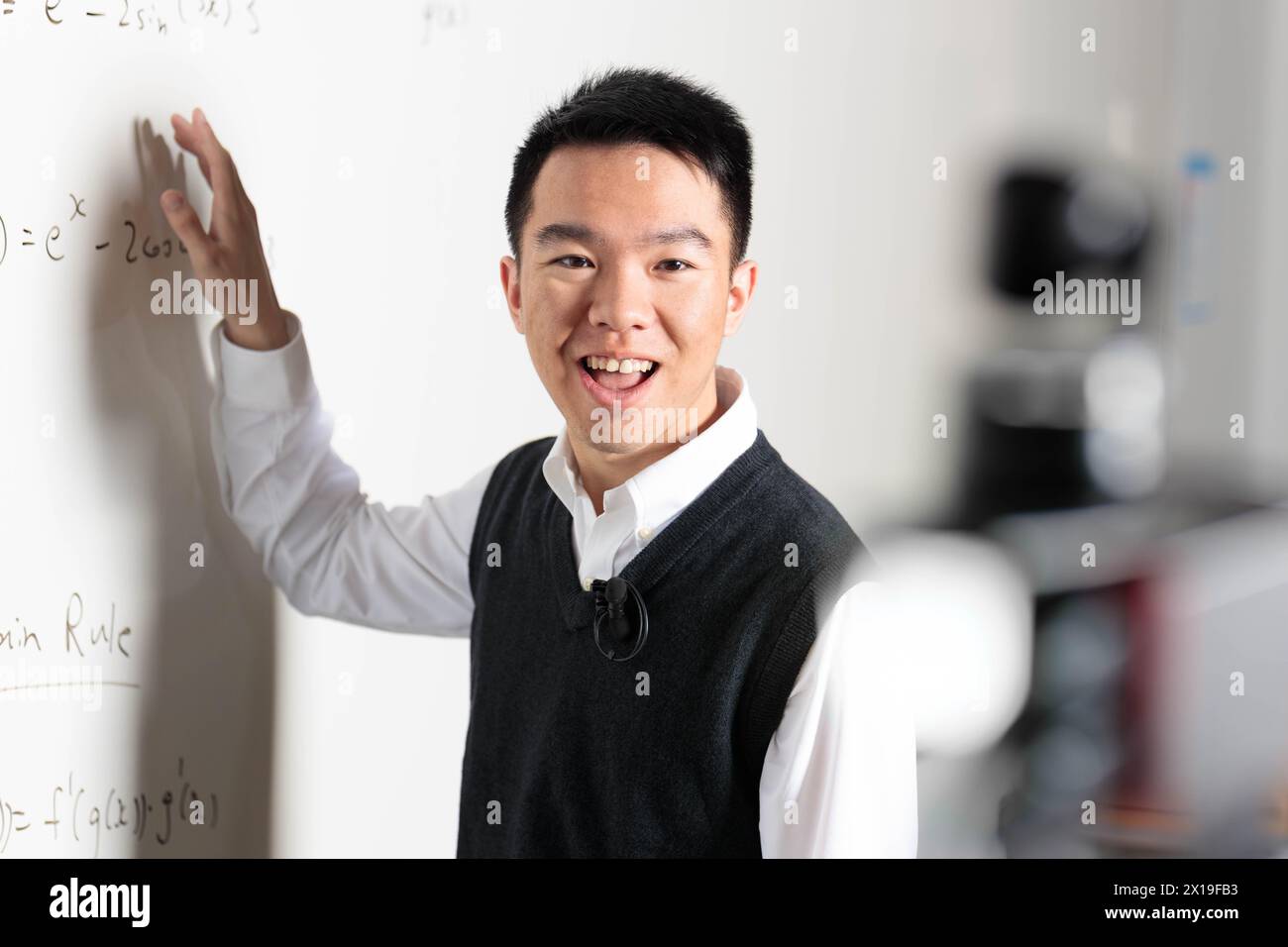 Un uomo in abito formale con una camicia e maniche arrotolate è felice di fare gesti sulla lavagna bianca, con un sorriso sul viso e il pollice rivolto verso l'alto Foto Stock