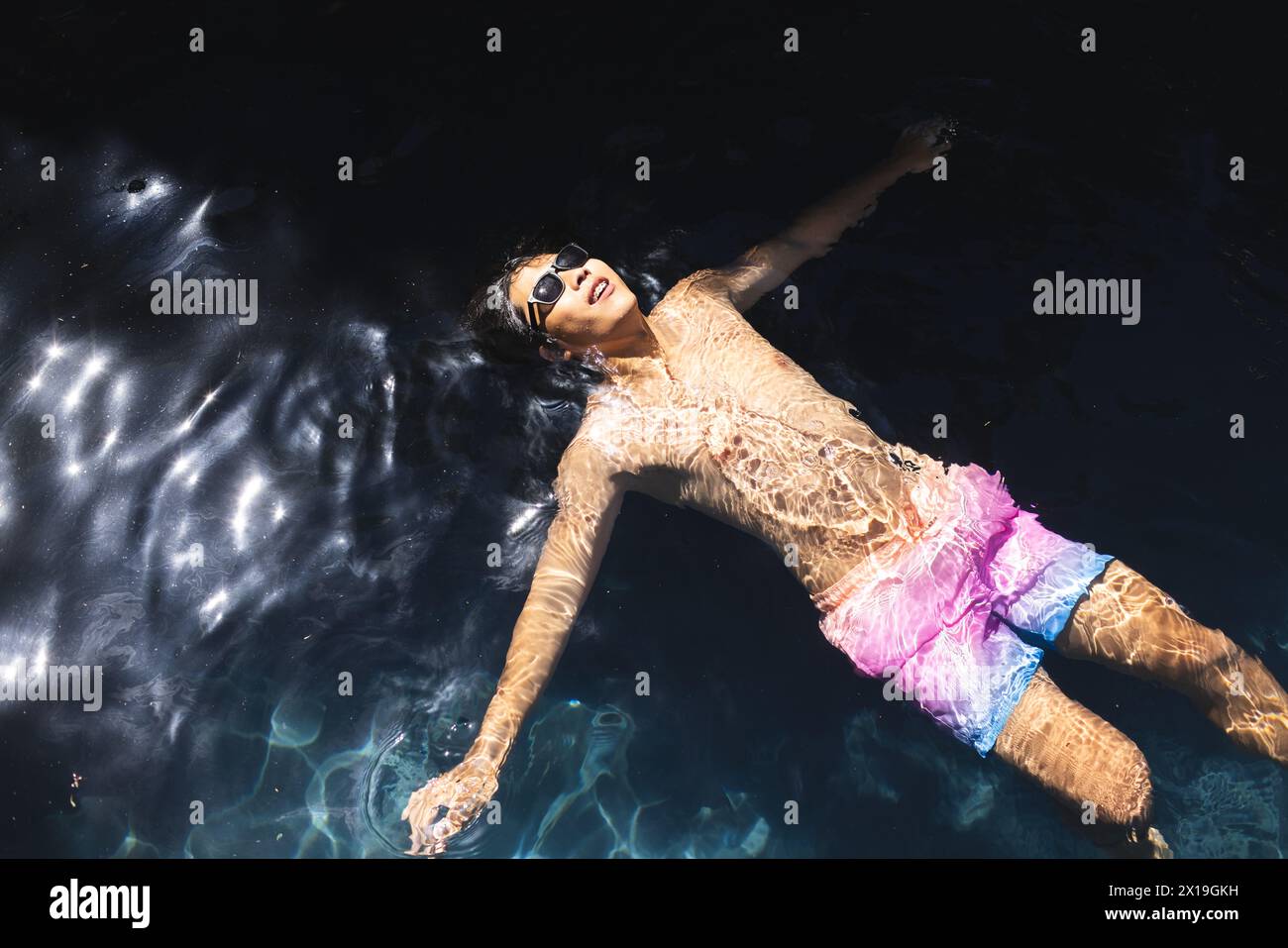 Un adolescente asiatico galleggia in acqua fuori a casa, indossando occhiali da sole, spazio copia Foto Stock