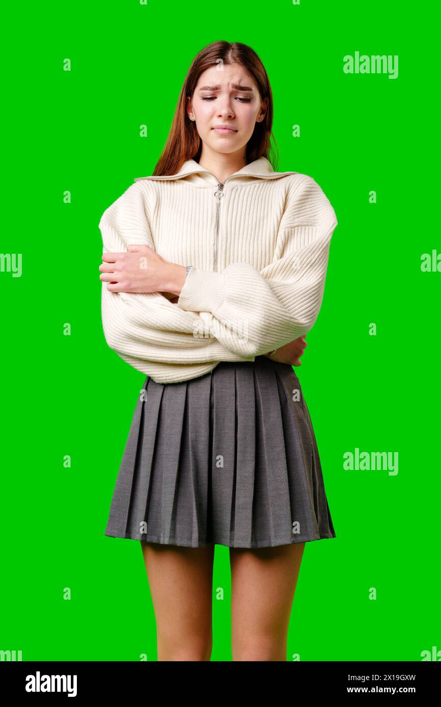 Giovane donna che sente freddo con il pullover bianco e la gonna grigia su sfondo verde Foto Stock