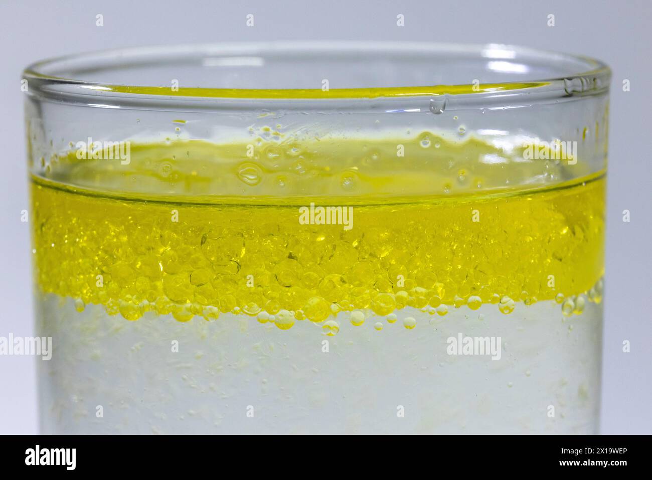 Primo piano di uno strato di goccioline d'olio che galleggiano fino alla sommità dell'acqua in un bicchiere Foto Stock