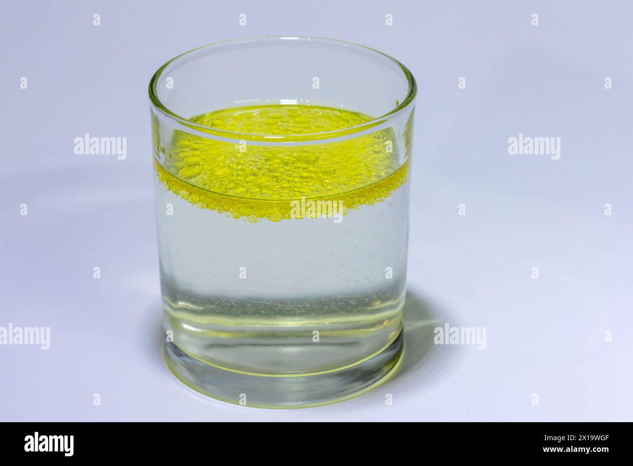 Olio miscelato in un bicchiere con acqua che indica che l'acqua e l'olio si separano con l'olio che galleggia verso la parte superiore Foto Stock