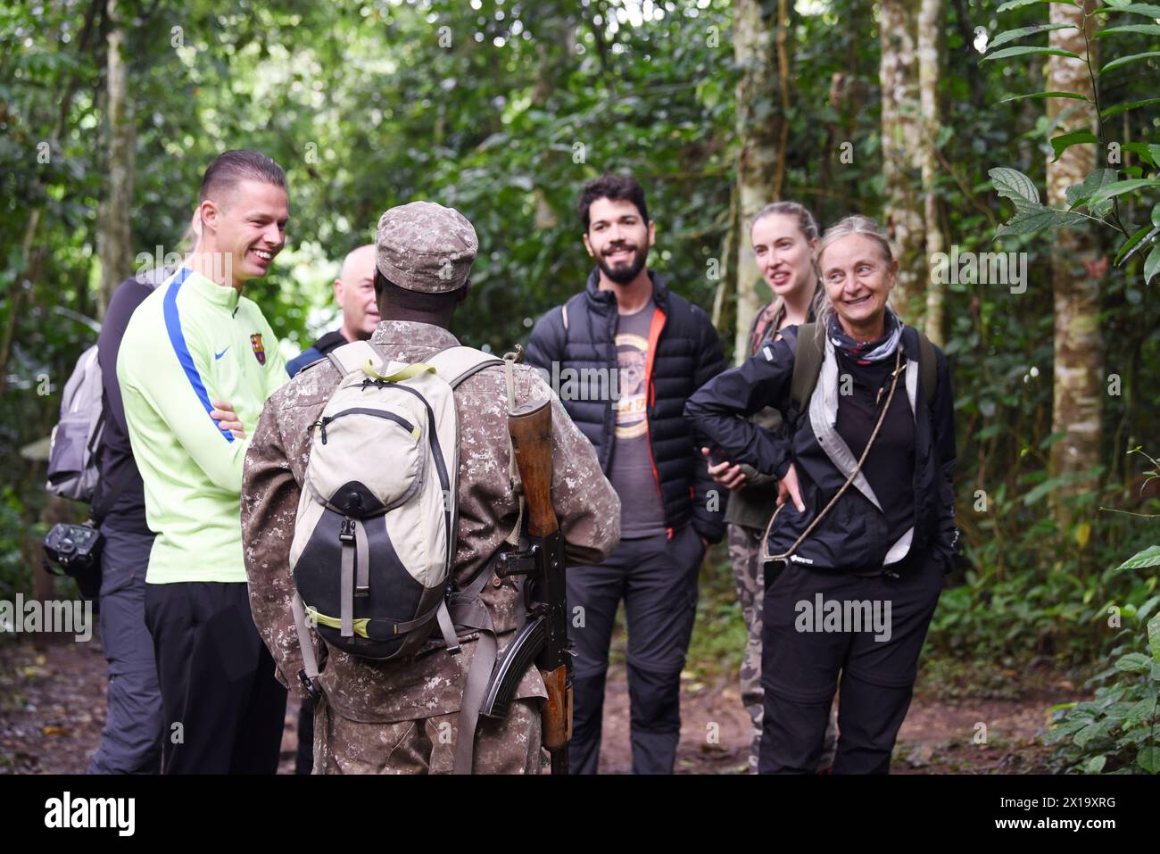 Nel mezzo della lussureggiante vegetazione del Parco Nazionale di Kibale, i turisti che indossano un abbigliamento da safari si impegnano in un briefing informativo condotto dalla loro guida armata, preparandosi Foto Stock
