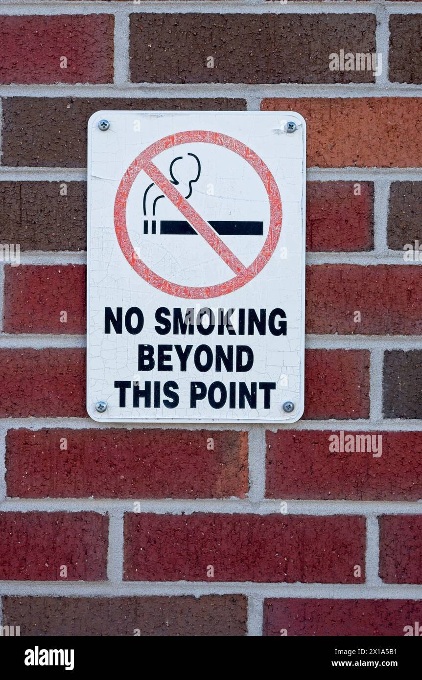 Sbiadito e crepato un cartello di divieto di fumo su un muro di mattoni Foto Stock