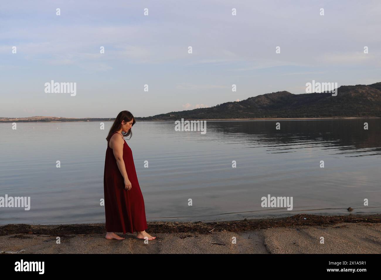 Donna elegante a piedi nudi in abito rosso che cammina godendosi lo stile di vita sulla spiaggia. fate una passeggiata, promenade. Foto Stock