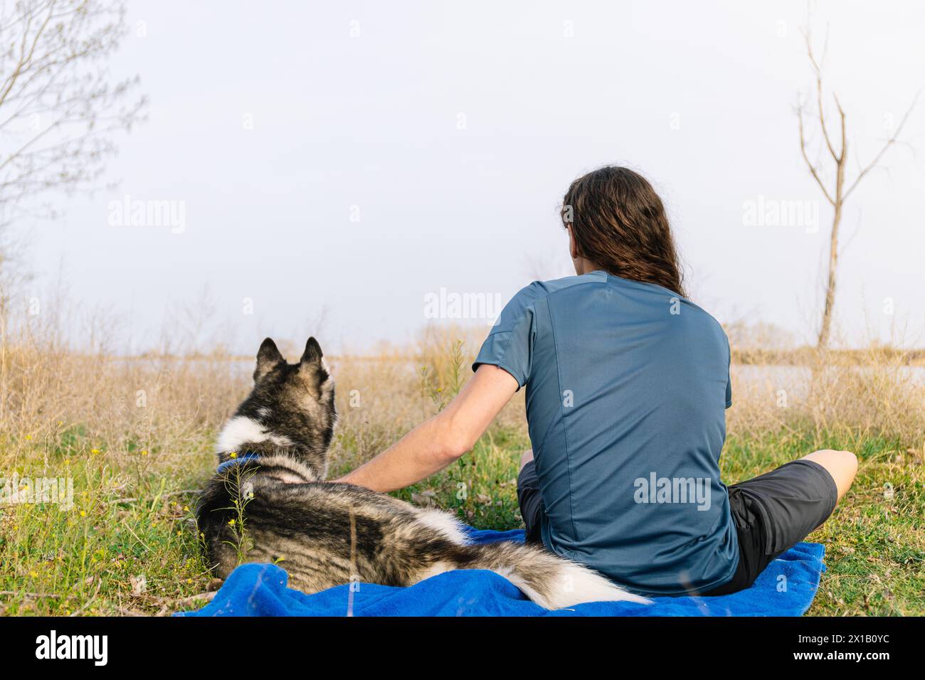 Foto orizzontale un uomo e il suo husky si siedono dietro, godendosi la vastità del paesaggio lungo il fiume in un momento tranquillo e riflessivo togeth Foto Stock