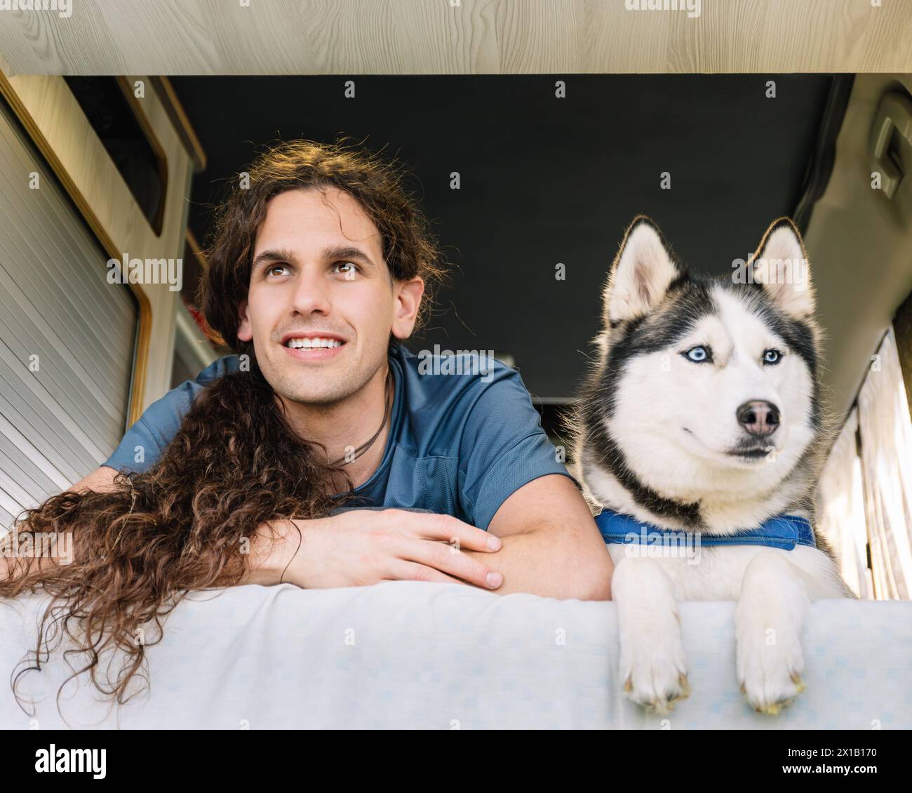 Foto orizzontale un uomo e il suo husky guardano fuori dal loro camper, affrontano pieni di attesa per la prossima tappa del loro viaggio, incarnando il Foto Stock