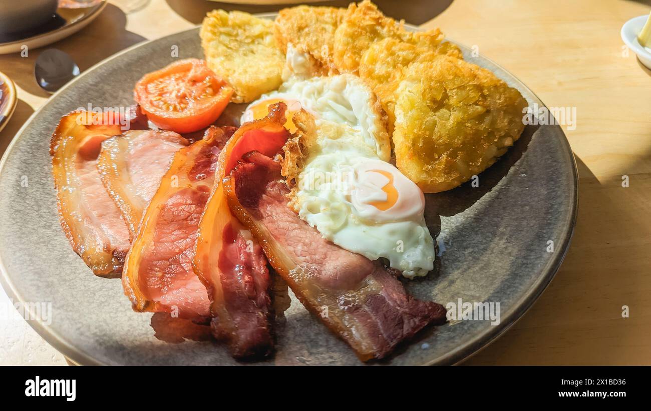 Colazione inglese tradizionale con pancetta, uova, pomodoro e crocchette di patate Foto Stock