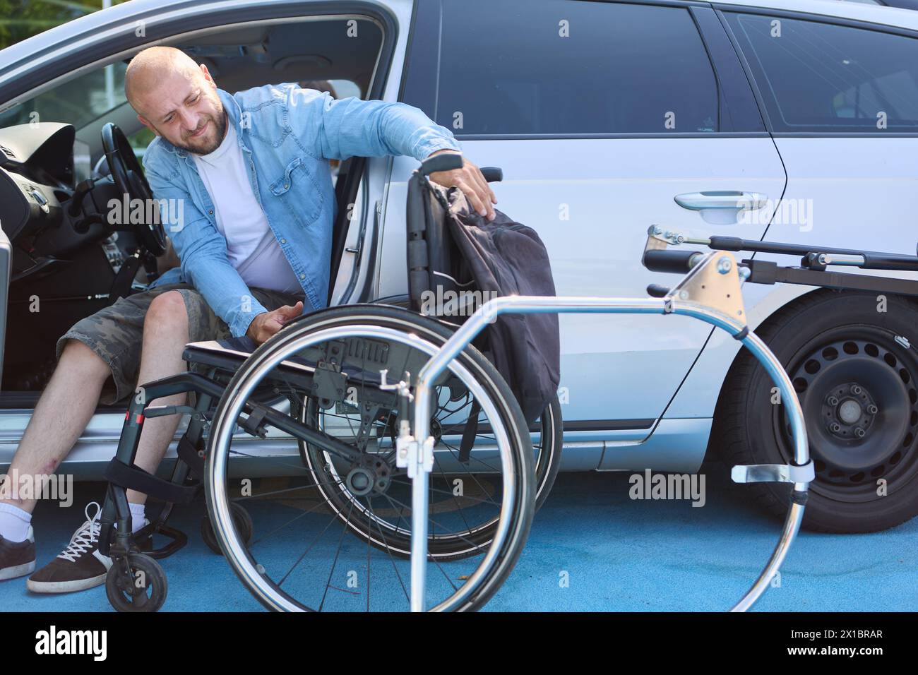 Una persona con disabilità viene vista trasferirsi dal suo seggiolino alla sua sedia a rotelle, dimostrando indipendenza e facilità con gli ausili alla mobilità. Foto Stock