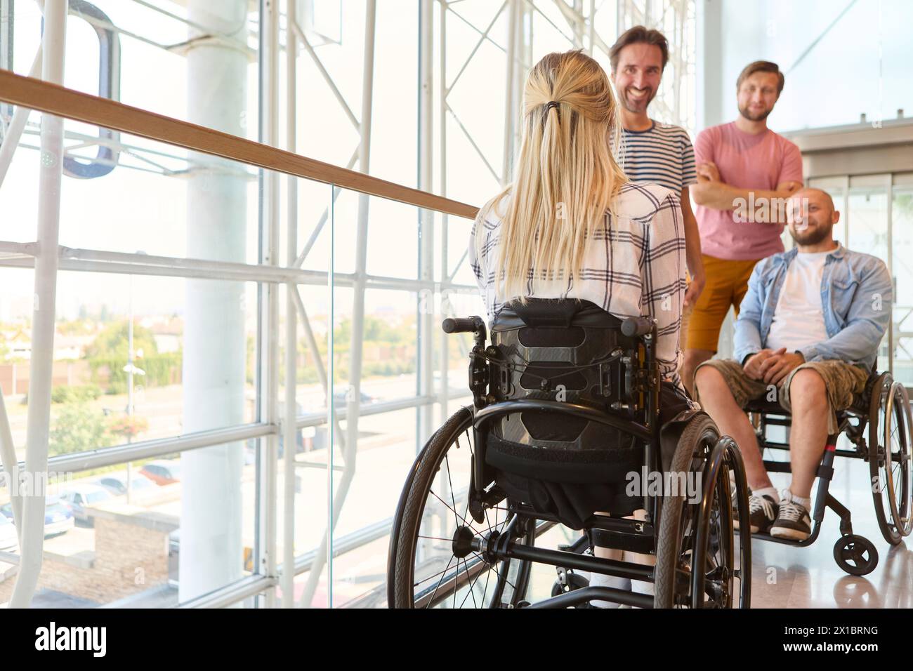 Un gruppo eterogeneo di persone, comprese persone su sedia a rotelle, condivide un momento di gioia in uno spazio luminoso e moderno. Foto Stock