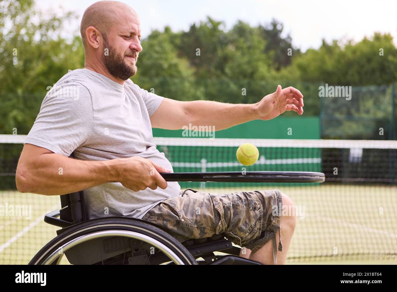 Una persona con disabilità che gioca a tennis su un campo all'aperto, esemplificando determinazione e divertimento negli sport adattivi. Foto Stock