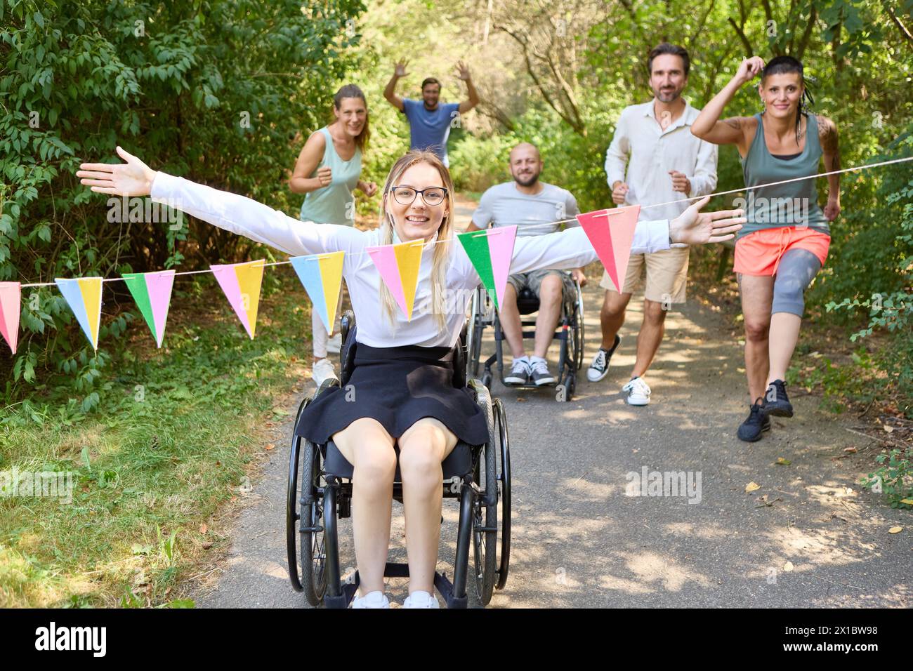 Un gruppo di amici felice che si diverte all'aperto con due persone su sedia a rotelle a guidare il divertimento. Foto Stock
