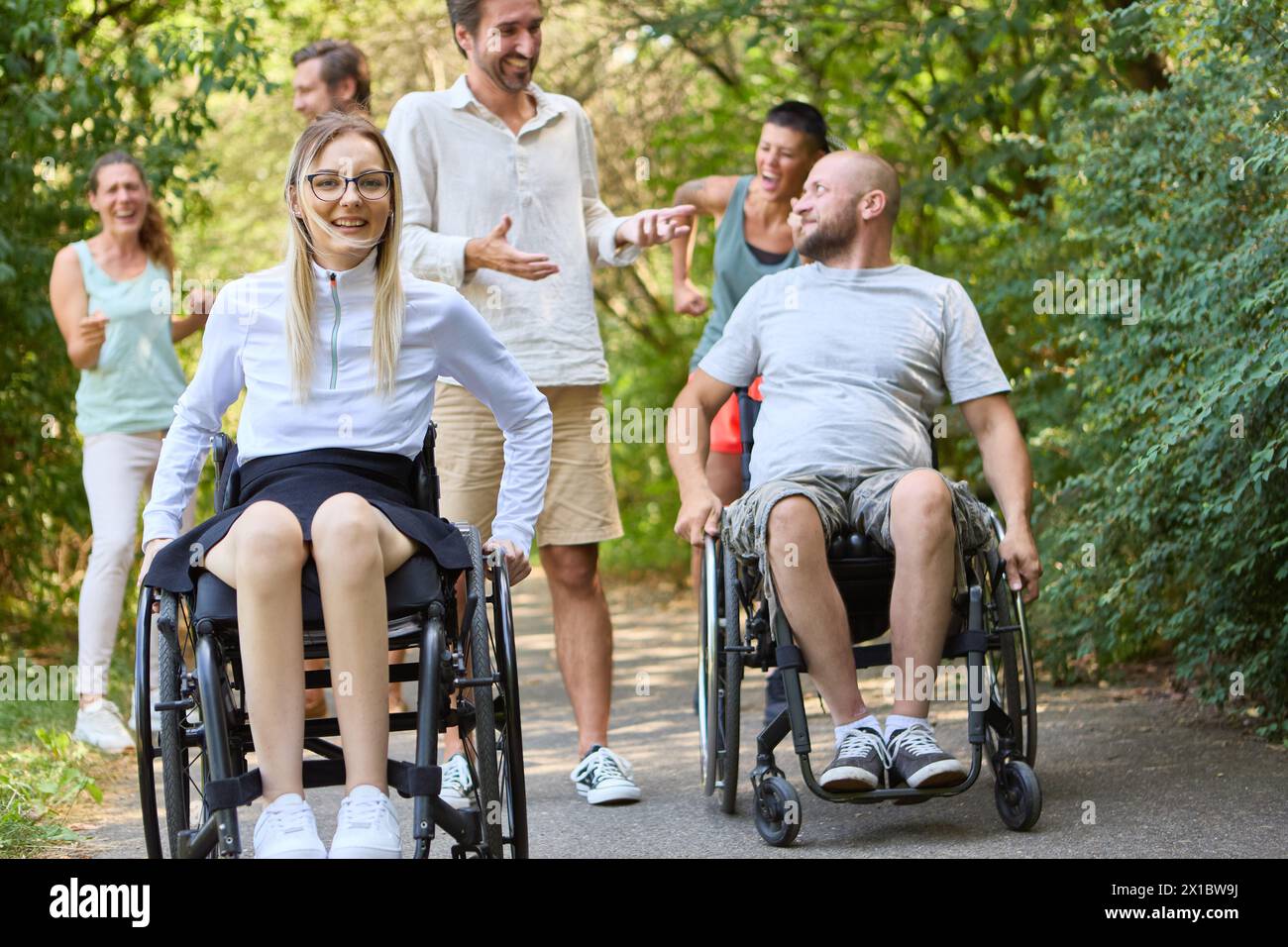 Un gruppo eterogeneo di persone, comprese persone su sedia a rotelle, trascorrono felicemente del tempo insieme in un parco. Foto Stock