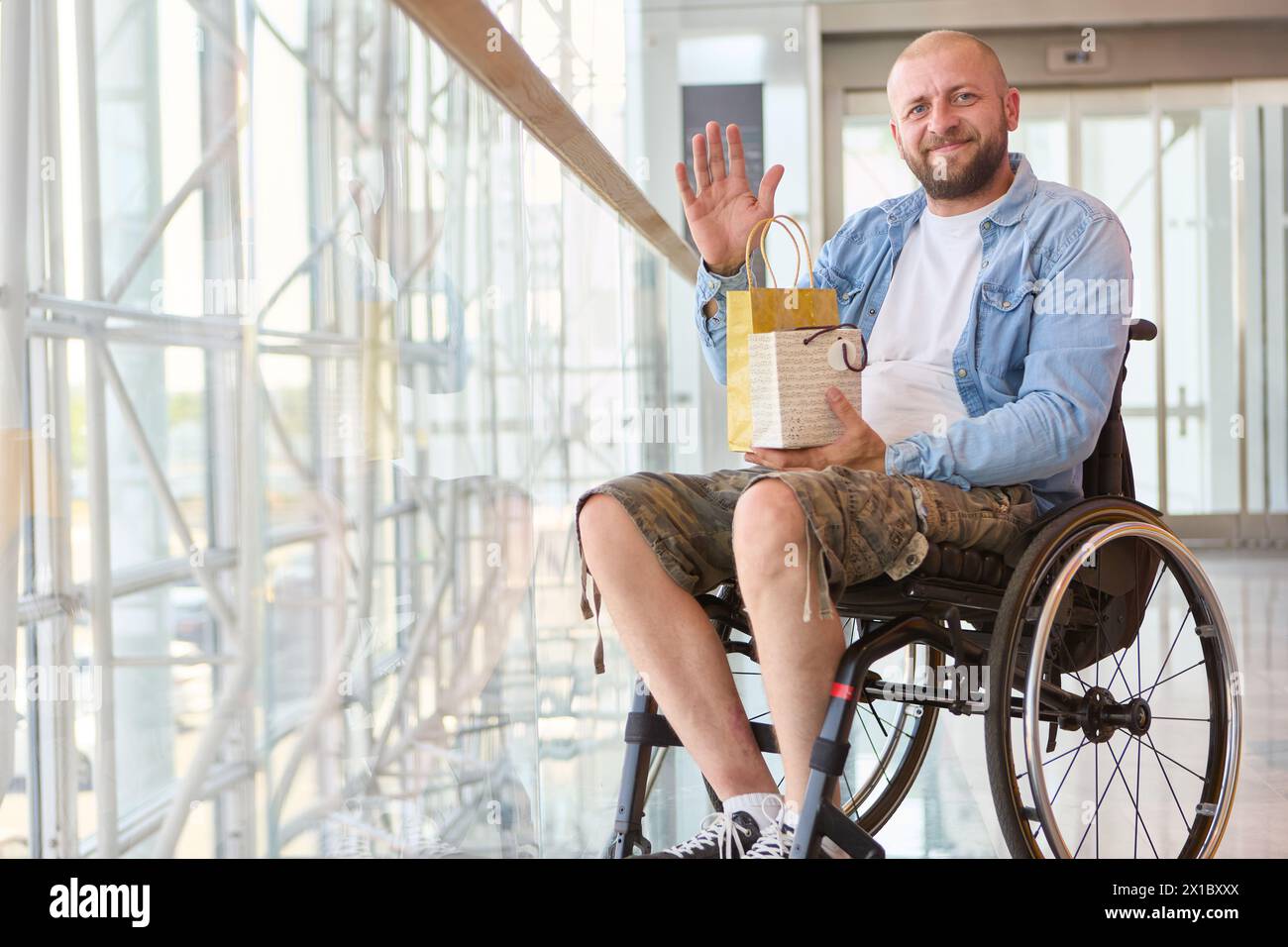 Una persona allegra che usa le onde di una sedia a rotelle mentre regge un regalo, esemplificando l'inclusività e la positività in un ambiente interno moderno. Foto Stock