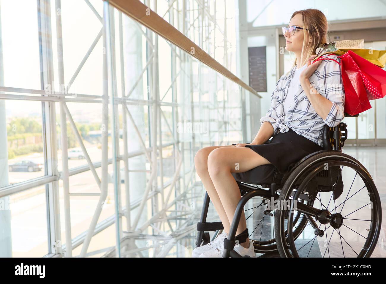 Persona sicura in sedia a rotelle che si diverte a fare shopping da sola, mostrando indipendenza e accessibilità in un ambiente da centro commerciale Foto Stock