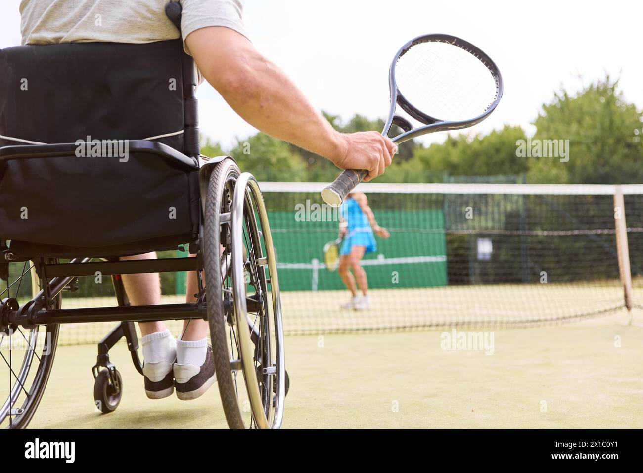 Un'immagine dinamica di una persona che utilizza una sedia a rotelle che partecipa attivamente a una partita di tennis, evidenziando l'accessibilità e l'inclusione negli sport. Foto Stock