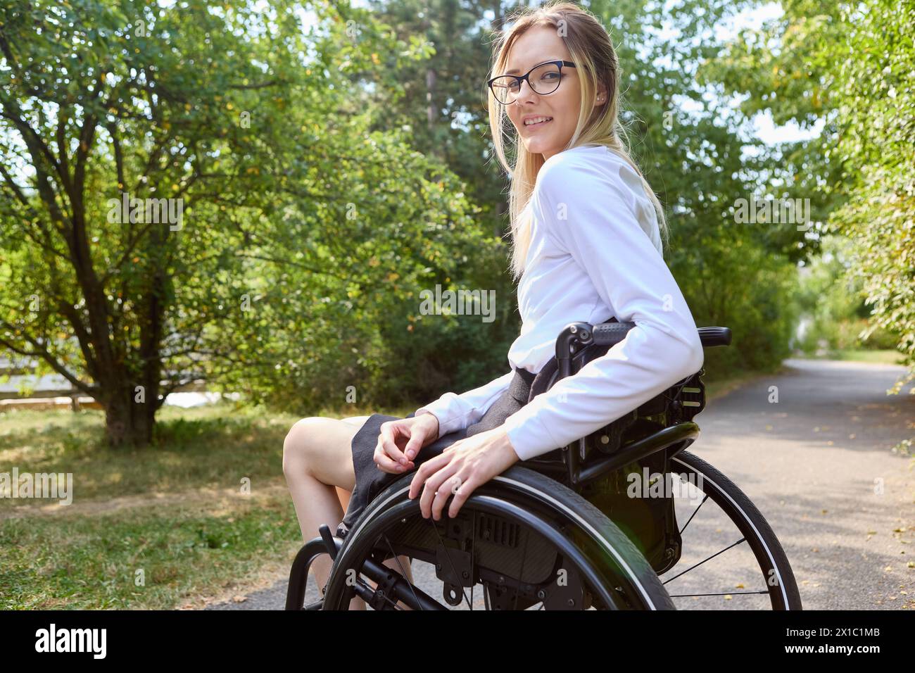 Donna sorridente in sedia a rotelle che vive all'aperto, promuovendo l'inclusione e l'accessibilità della disabilità. Foto Stock