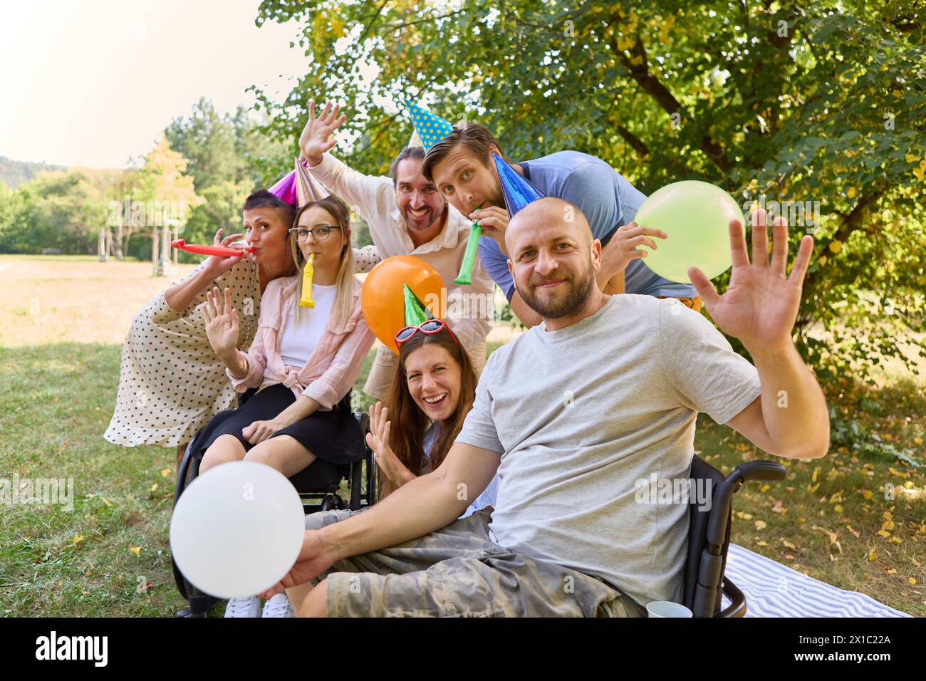 Gruppo di amici felici con accessori per feste che si godono una festa all'aperto inclusiva, con una donna in sedia a rotelle in prima linea Foto Stock