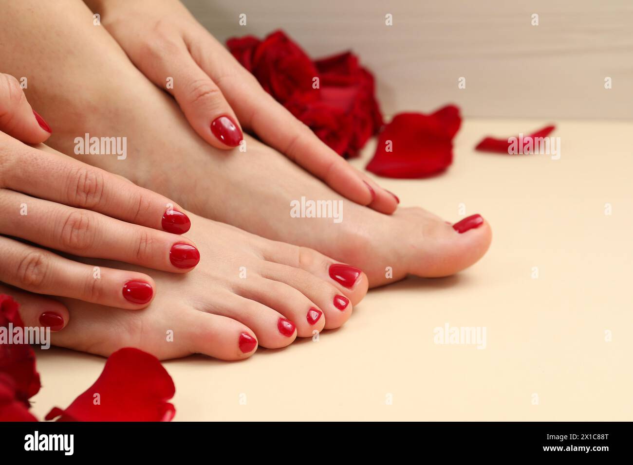 Donna con eleganti unghie rosse dopo la procedura di pedicure e petali di rosa su sfondo beige, primo piano Foto Stock