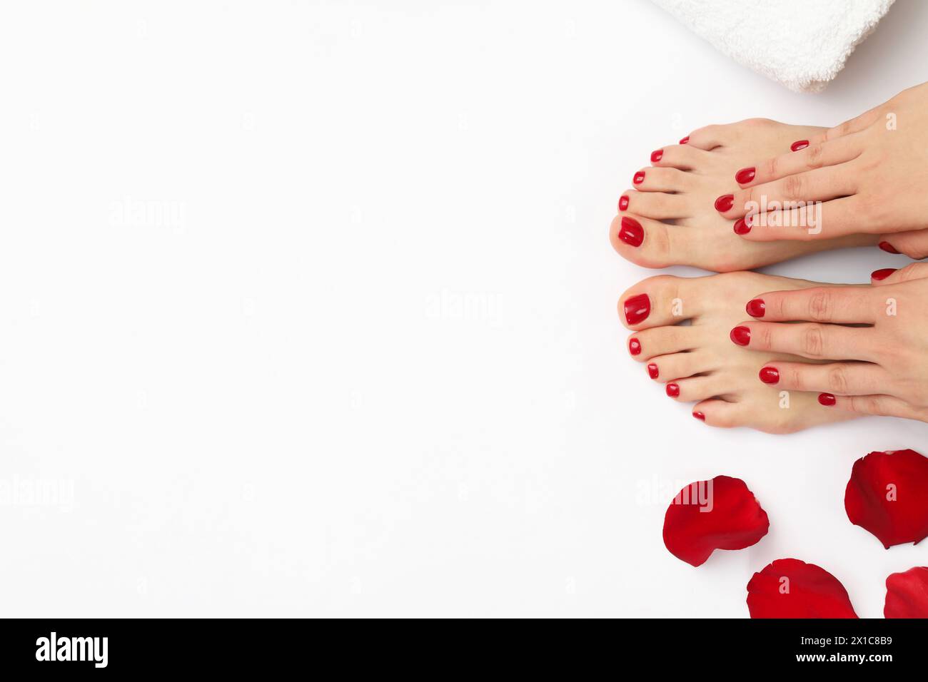 Donna con eleganti unghie rosse dopo la pedicure e petali di rosa su sfondo bianco, vista dall'alto. Spazio per il testo Foto Stock