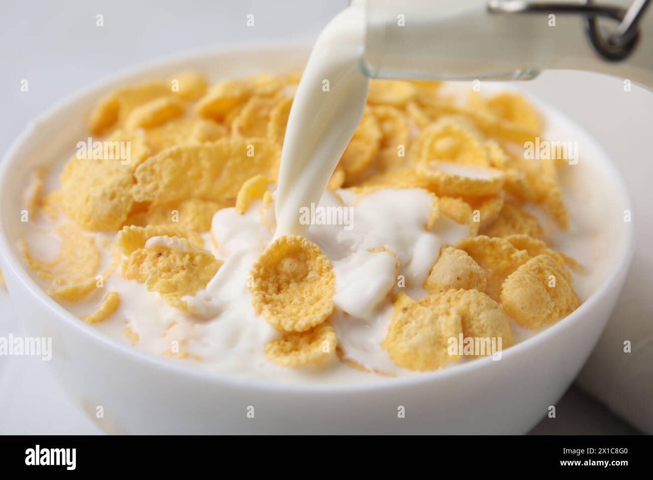 Cereali da colazione. Versare il latte nel recipiente con gustosi granoturco al tavolo, primo piano Foto Stock