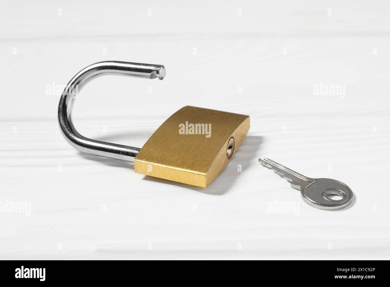 Lucchetto in acciaio con chiave su tavolo in legno bianco, primo piano Foto Stock