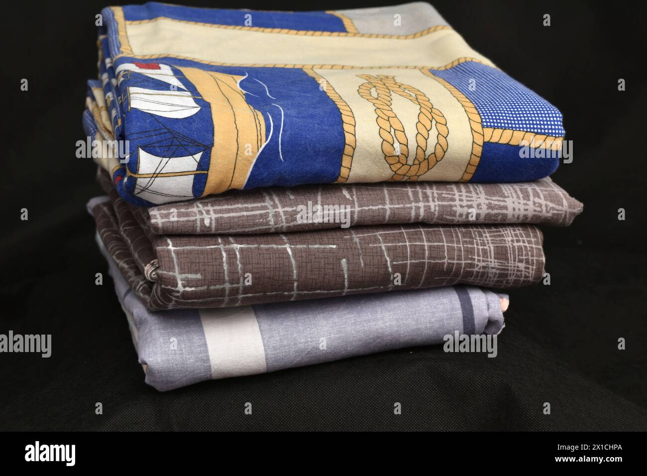 Primo piano di una pila di biancheria da letto, lenzuola, federazioni su sfondo scuro. Foto Stock