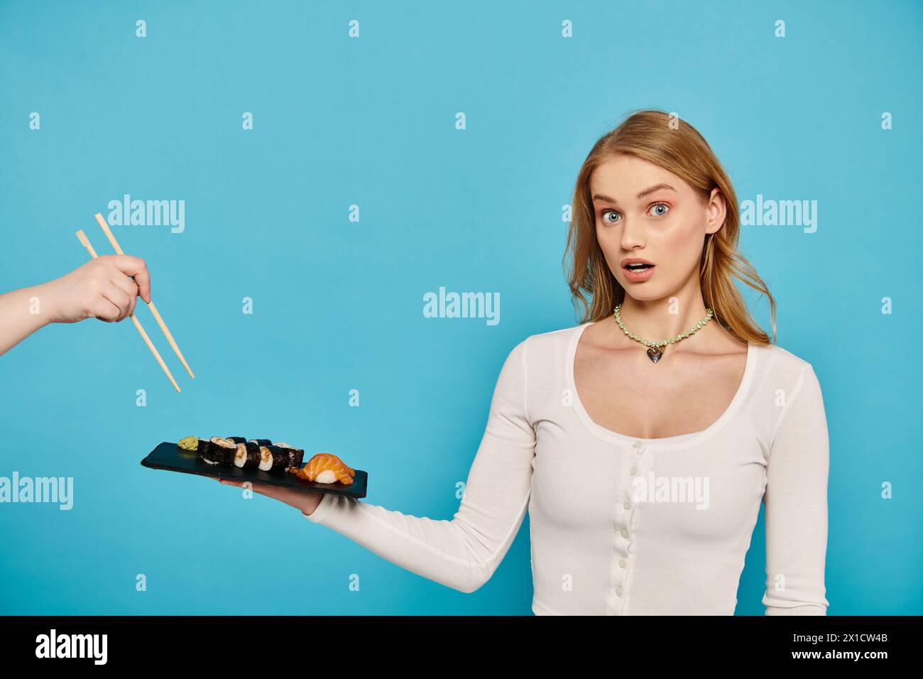 Donna bionda che tiene con grazia un piatto di sushi e bacchette, mostrando delizie culinarie e apprezzamento culturale. Foto Stock