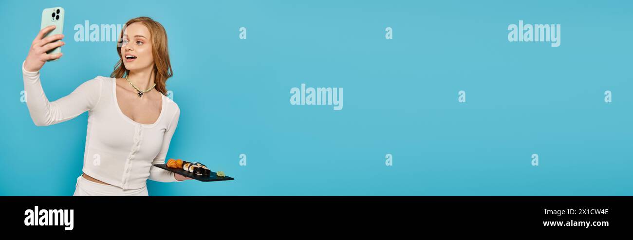 Una splendida donna bionda cattura un momento con il suo cellulare mentre posa con deliziosi piatti asiatici. Foto Stock