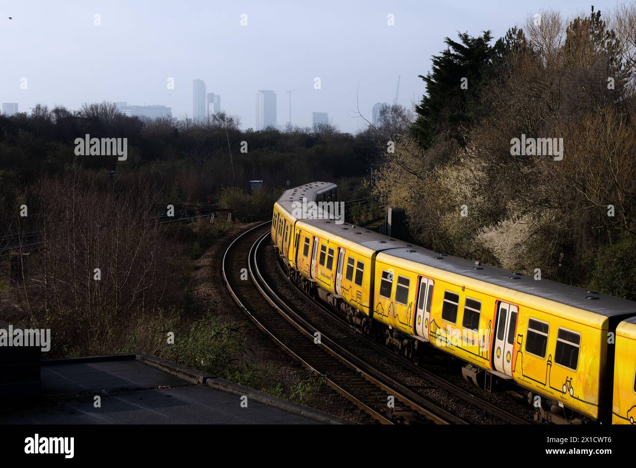 Treno Merseyrail che viaggia attraverso il paesaggio boscoso con lo skyline della città di Liverpool sullo sfondo Foto Stock