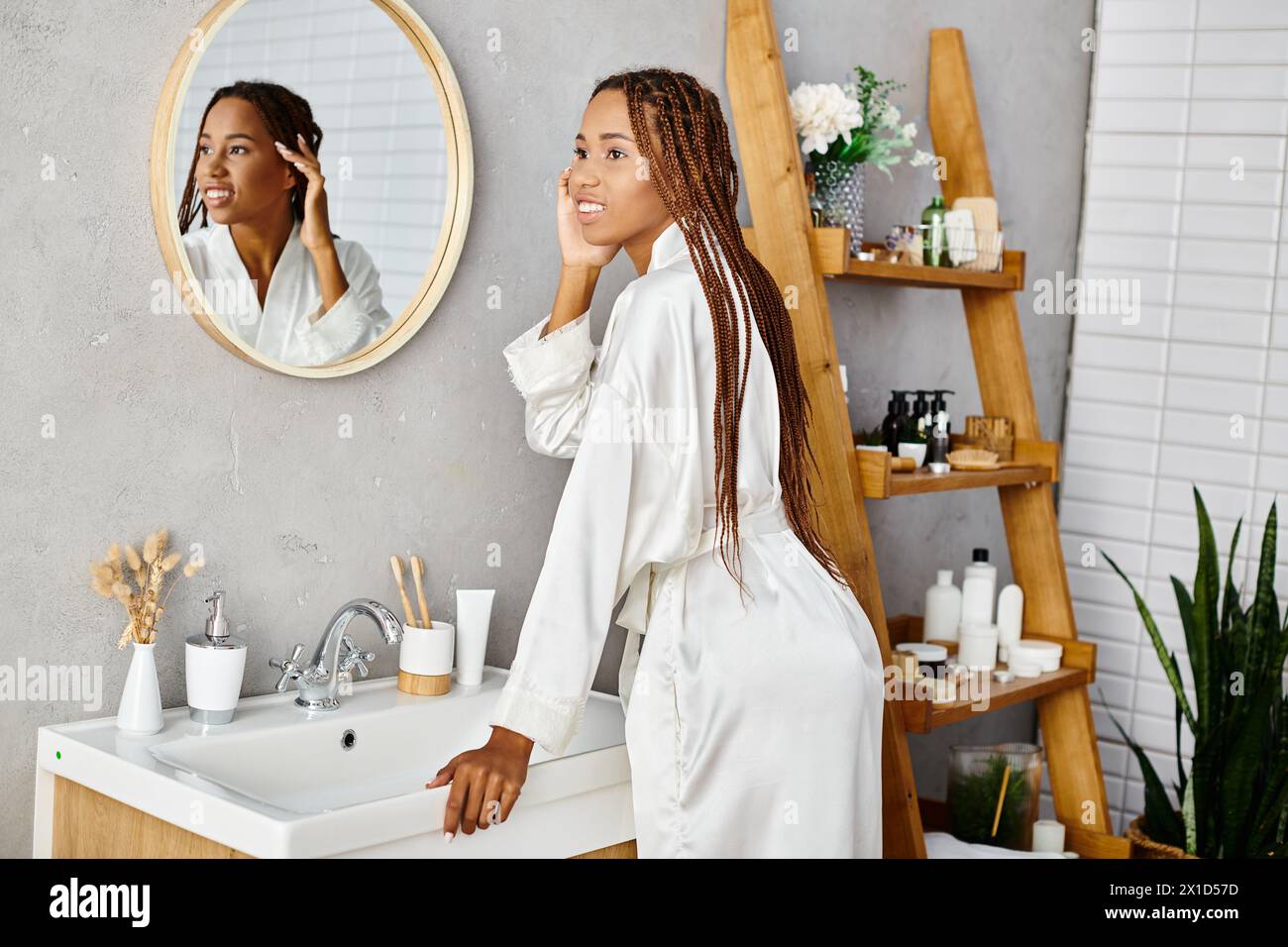 Una donna afroamericana con trecce afro si trova di fronte a uno specchio in un bagno moderno Foto Stock